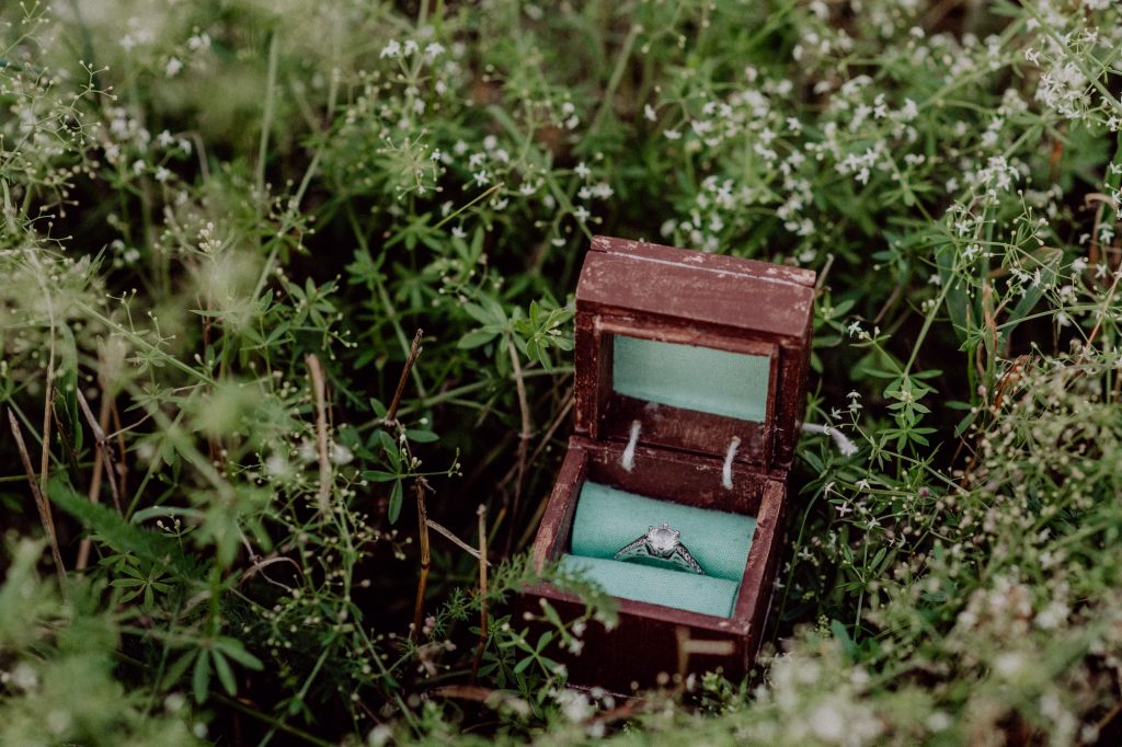An engagement ring in a wooden box on grass.