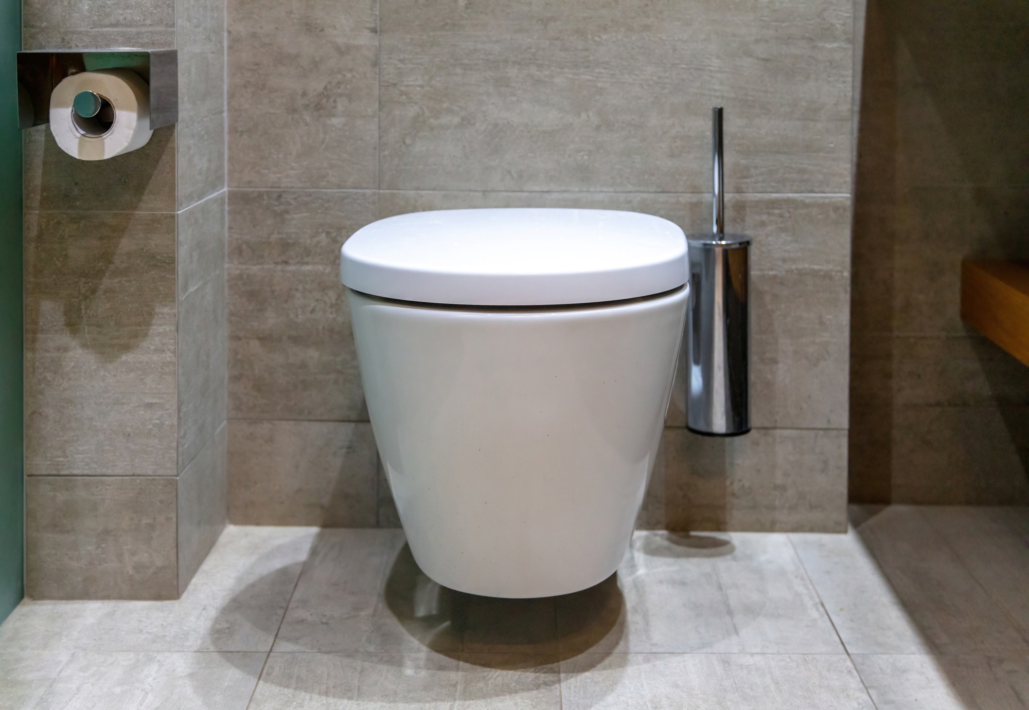 Modern toilet interior design, hanging toilet bowl and brush, tiled walls and floor.